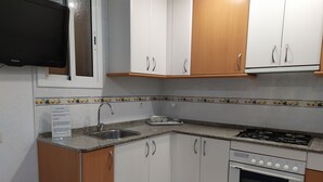 Una cocina con armarios blancos, encimera de granito, pileta de acero inoxidable, estufa a gas y horno.