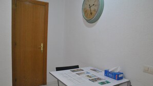Una habitación con una puerta de madera, una mesa blanca con papeles y una caja de pañuelos, y un reloj en la pared.