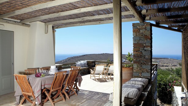 A covered outdoor dining area with a table set for four, stone pillars, and a view of the sea. - Premium Villa με 3 υπνοδωμάτια [150m2], Diles & Rinies Villas Tinos (Tinos)