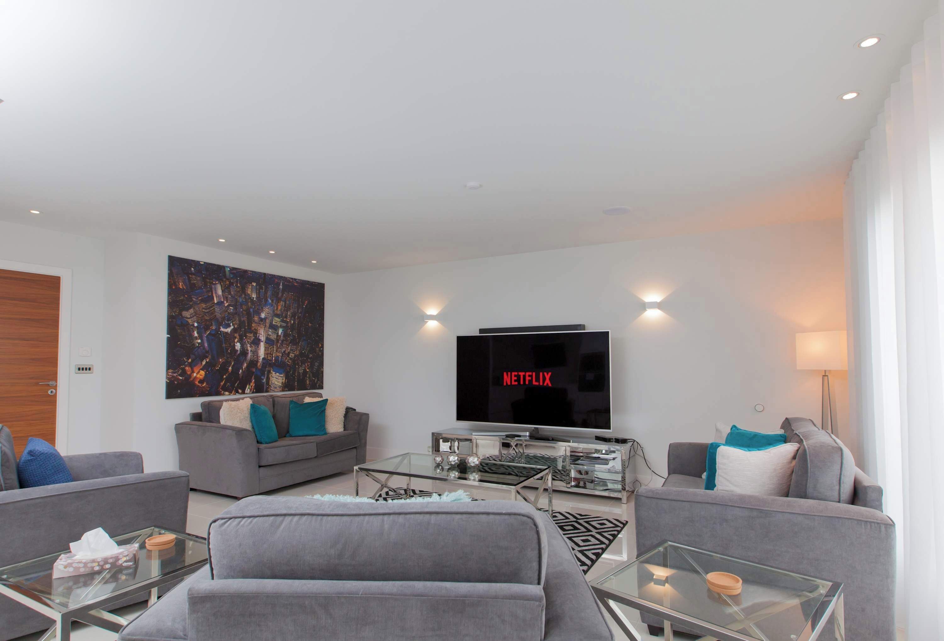 Uma sala de estar moderna com televisão de tela plana, sofás cinzas e mesas de centro de vidro.