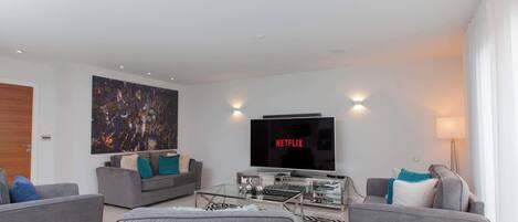 Een moderne woonkamer met een flatscreen televisie, grijze banken en glazen salontafels.