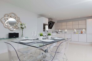 A modern kitchen with white cabinets, a glass dining table, and clear chairs.