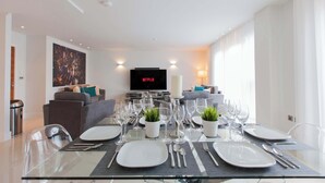 A modern living room with a dining area set for a meal, a television displaying 'NETFLIX,' and a sofa with cushions. - Luxurious Central Edinburgh Apartment - Sleeps 6 (Edinburgh)
