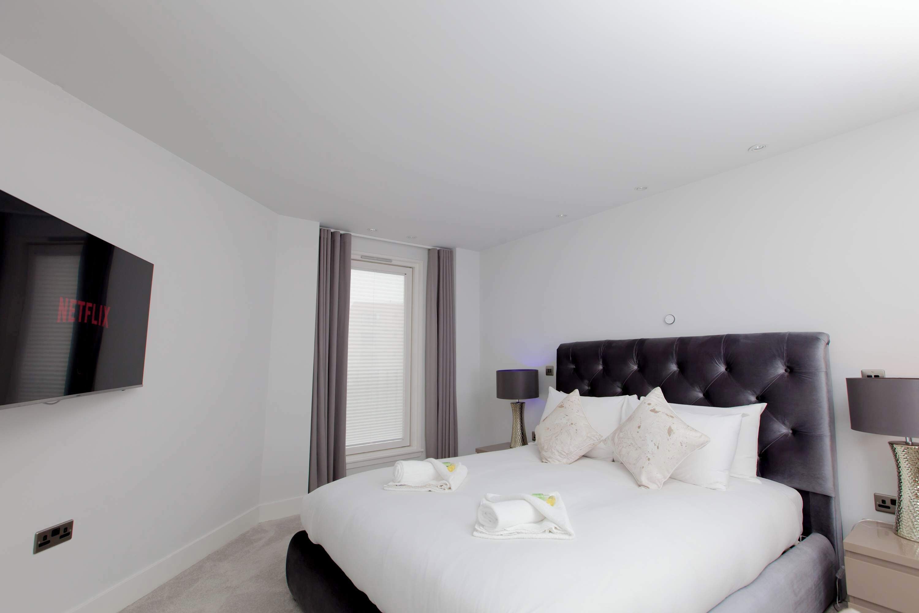 A hotel room with a large bed, a flat-screen TV, a window with curtains, and a bedside lamp.
