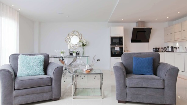 A modern living room with two grey sofas, a glass coffee table, and a kitchen area with white cabinets and appliances. - Luxurious Central Edinburgh Apartment - Sleeps 6 (Edinburgh)