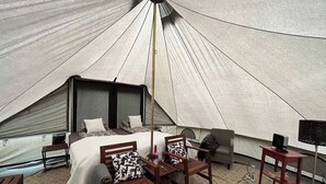 A tented accommodation with a bed, two wooden chairs, a small table, and a television. - Godaland Guesthouse (Rangárþing eystra)