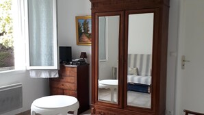 Ein Zimmer mit einem großen Holzschrank, einem weißen runden Tisch, einem Stuhl und einem Bett mit gestreifter Decke.