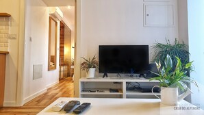 Un salon moderne avec un téléviseur à écran plat, une table basse avec des télécommandes et une plante en pot.