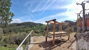 Une balançoire en bois rustique, installée sur un chemin de terre, offre une vue sur une colline boisée et un ciel dégagé.