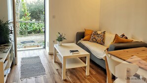 Un salon moderne avec un canapé, une table basse et une petite table sur laquelle est posée une plante. Une porte-fenêtre coulissante donne accès à un jardin.