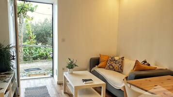 Een moderne woonkamer met een bank, een salontafel en een kleine tafel met een plant. Er is een schuifdeur die uitkomt op een tuin.