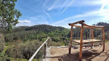 Une balançoire en bois rustique, installée sur un chemin de terre, offre une vue sur une colline boisée et un ciel dégagé.