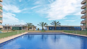 Una piscina con superficie d'acqua cristallina e blu, circondata da una recinzione verde e palme.