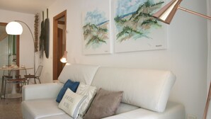 Un divano in pelle bianca con cuscini, una lampada da terra e due quadri appesi al muro.