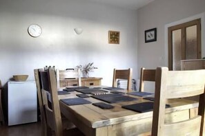 A dining area with a wooden table, chairs, a clock, and a refrigerator.