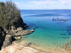 A coastal landscape with clear blue waters, rocky cliffs, and sparse vegetation.