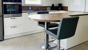 A modern kitchen with built-in appliances, a large window, and a central island with seating. - Villa Métisse with neat decoration and great comfort (Groix)