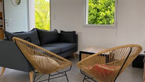 A modern living room with a grey sofa, two wicker chairs, a small wooden table, and a window with a view of greenery. - Villa Métisse with neat decoration and great comfort (Groix)