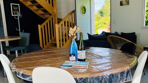 A round table with a plastic cover, surrounded by white chairs, a bottle of wine, and a small vase with dried flowers. - Villa Métisse with neat decoration and great comfort (Groix)
