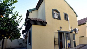 A two-story building with a yellow facade, a tiled roof, and a small balcony. - Chalet el Naranjo - Sevilla (Dos Hermanas)