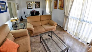 A living room with two sofas, a glass coffee table, and a dining area with a table and chairs. - Chalet el Naranjo - Sevilla (Dos Hermanas)