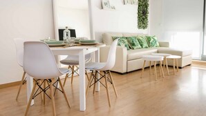 Ein modernes Wohnzimmer mit Essbereich, ausgestattet mit einem weißen Sofa, einem Esstisch mit Stühlen und einer grünen Pflanzenwand.