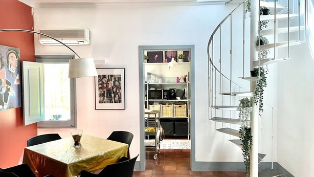 Un espace repas comprenant une table et des chaises, un escalier avec une rampe et une étagère contenant divers objets.