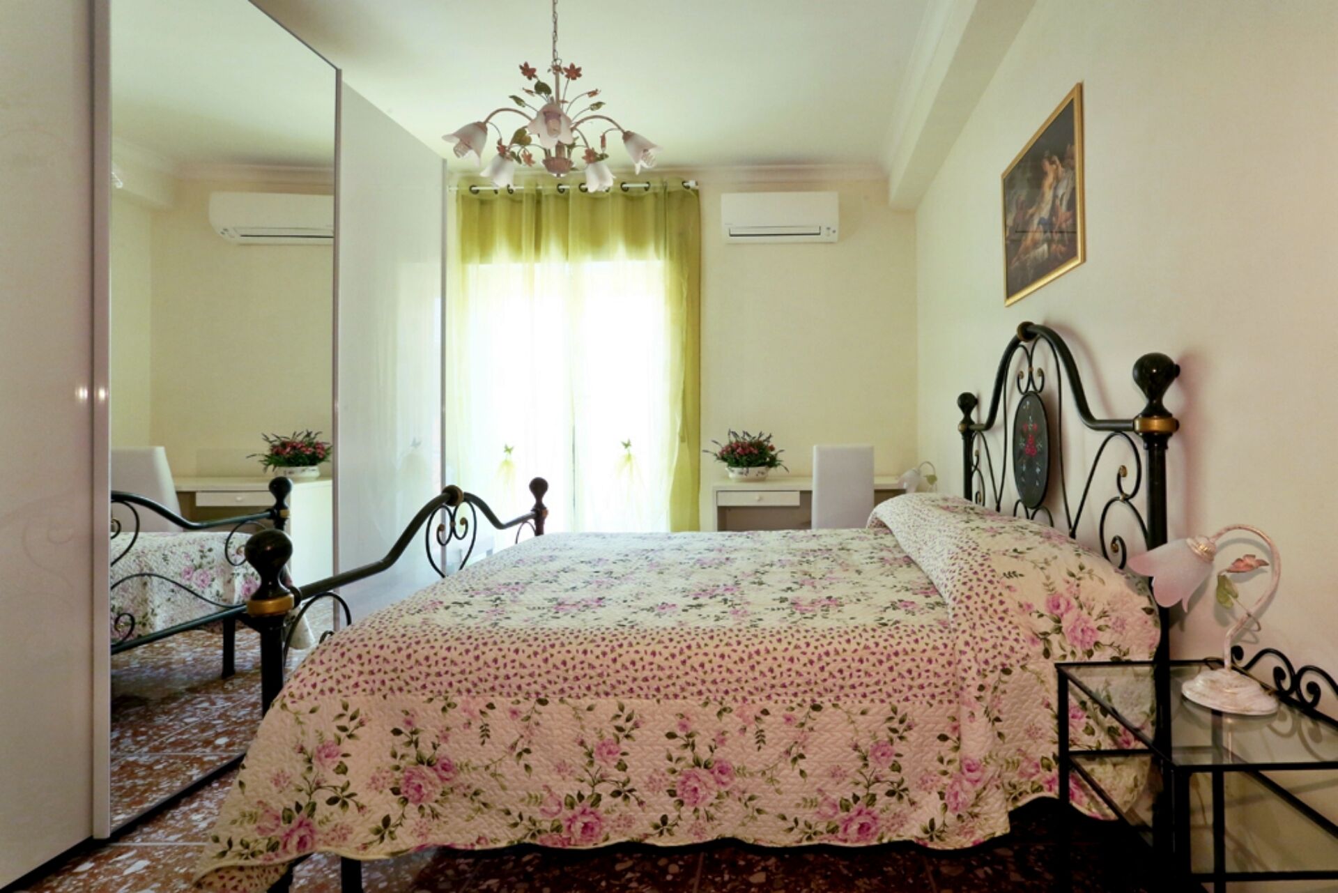 Een slaapkamer met een bed, een spiegel, een kroonluchter en een schilderij aan de muur.