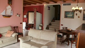 Una sala de estar acogedora con un sofá, una mesa de comedor con sillas, una escalera y una araña.