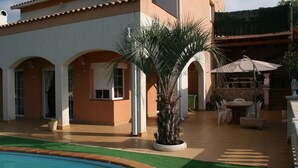 Zona de piscina con palmera, asientos exteriores y pared de piedra.