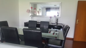 Un coin repas avec une table en verre, des chaises noires, un miroir et une porte.