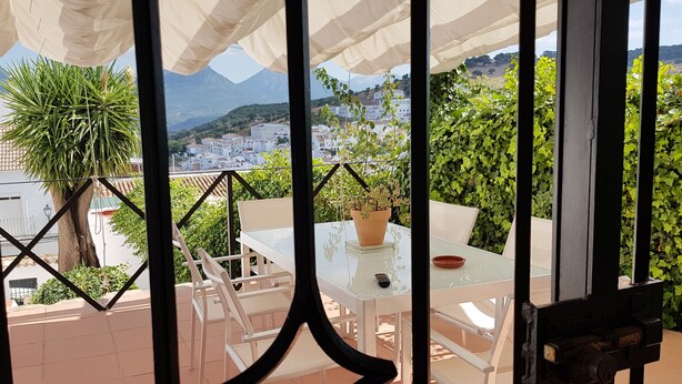 Eine Terrasse mit einem Glastisch und Stühlen, einem Blumentopf und Blick auf eine Stadt und Berge.