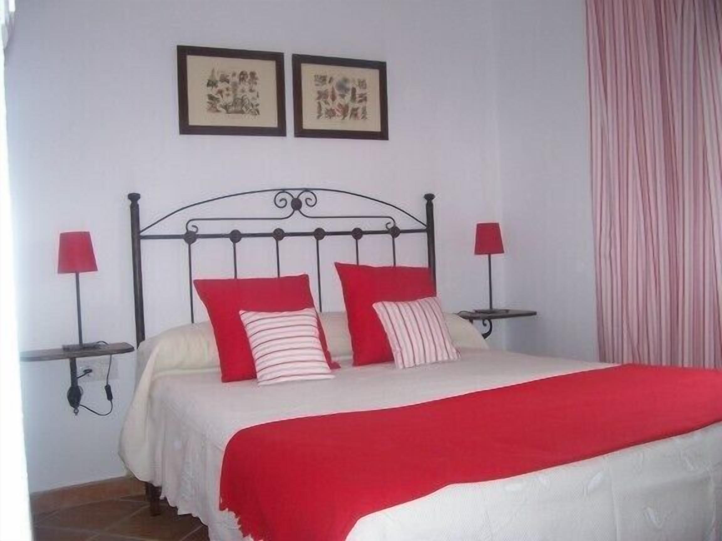Een bed met een metalen frame, twee nachtkastjes met lampen, en twee ingelijste foto's aan de muur.