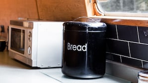 Una cocina con microondas, un recipiente para pan y una ventana con vistas a edificios.