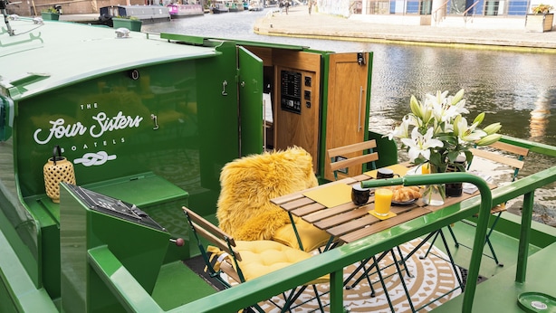 Un bote verde con un área de estar acogedora que incluye un sillón amarillo de pelo, una mesa de madera con un florero y un menú.