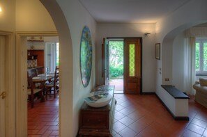 Un hall spacieux comprenant un coin repas, un grand vase décoratif posé sur un piédestal en bois, et une vue sur l’extérieur grâce à une porte vitrée.