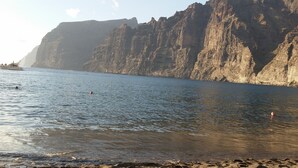 Ein Strand mit einer felsigen Klippe und einem Boot im Wasser.