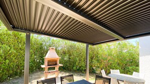 Eine Terrass mit Grill aus Ziegelsteinen, einem Tisch und Stühlen.