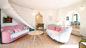 Ein geräumiges Wohnzimmer mit Treppe, zwei Sofas, einem runden Couchtisch und einem Essbereich mit Stühlen und Tisch.