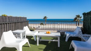 Una terraza con mobiliario blanco de plástico, una mesa con fruta y vistas a la playa y al océano.