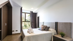 Un dormitorio con una cama grande, una mesita de noche, una planta en maceta y vistas al exterior.