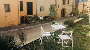 A courtyard with a table and two chairs, a green door, and a staircase leading to a building with a tiled roof. - Charming, centrally located house close to Carcassonne, perfect for families! (Capendu)