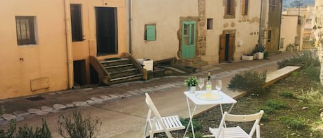 A courtyard with a table and two chairs, a green door, and a staircase leading to a building with a tiled roof.