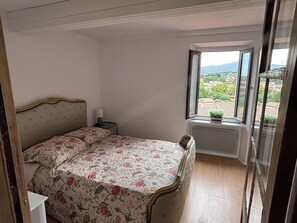 Une chambre à coucher avec un lit, une table de chevet, une fenêtre donnant sur un paysage agréable et un radiateur.