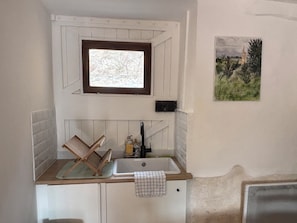 A small kitchenette with a window, a sink, and a towel hanging on the cabinet.