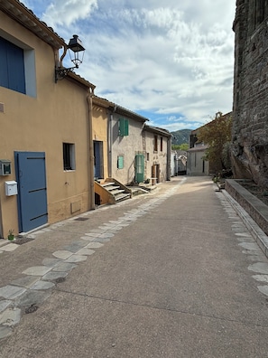 Une rue étroite, bordée de bâtiments des deux côtés, avec des marches en pierre et une porte bleue.