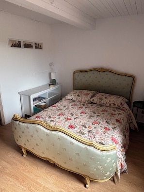 Une chambre à coucher avec un lit de style vintage, une table de chevet avec une lampe et une petite étagère avec des livres.