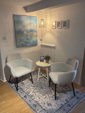 Une pièce comprenant deux fauteuils, une petite table avec une plante, un tableau et un luminaire fixé au mur.