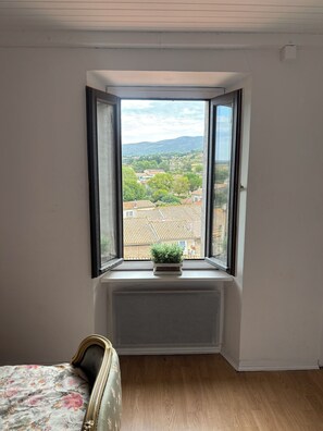 Une chambre avec un lit, un radiateur et une fenêtre donnant sur une ville et des montagnes.