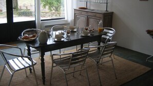Een eetruimte met een tafel voor vier personen, een raam met uitzicht op groen en een plank met glazen.